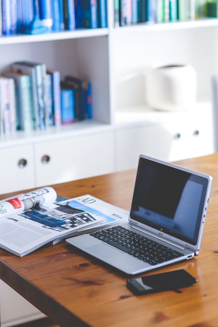 about-02 A stylish desk setup featuring a laptop, magazine, and bookshelf in a contemporary home office.