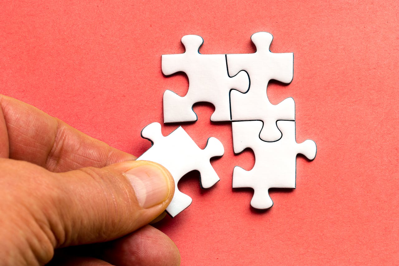 Close-up of a hand assembling white jigsaw puzzle pieces on a red background.